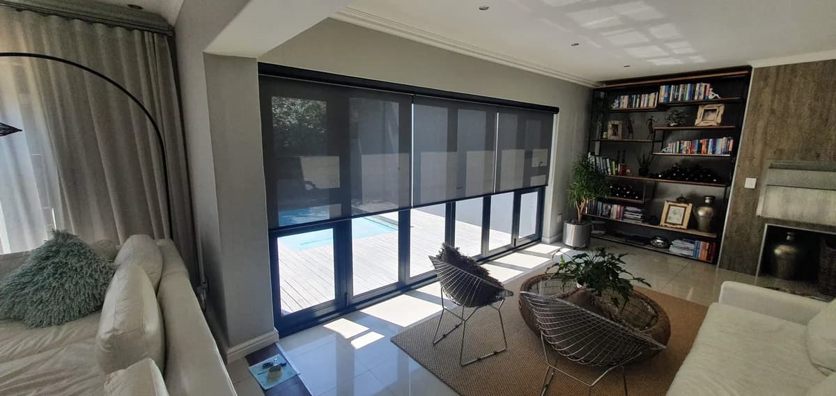 Dark perforated screen roller blind in a lounge overlooking a pool