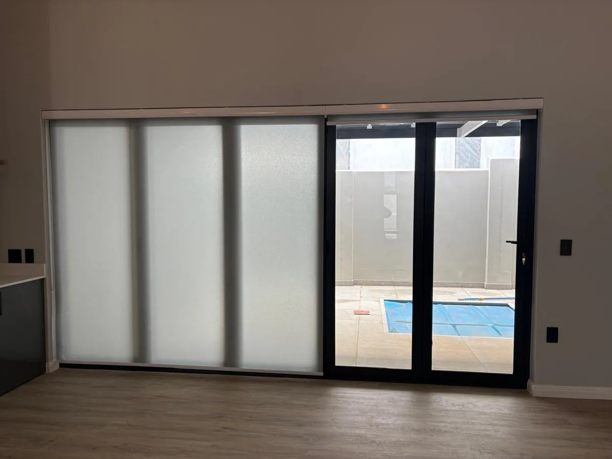 Translucent roller blind fully blocking the view over a sliding door beside a pool