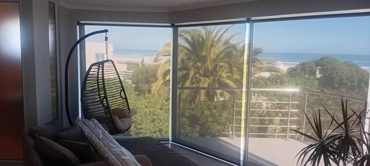 Perforated screen roller blinds on a balcony with a palm tree and beach view