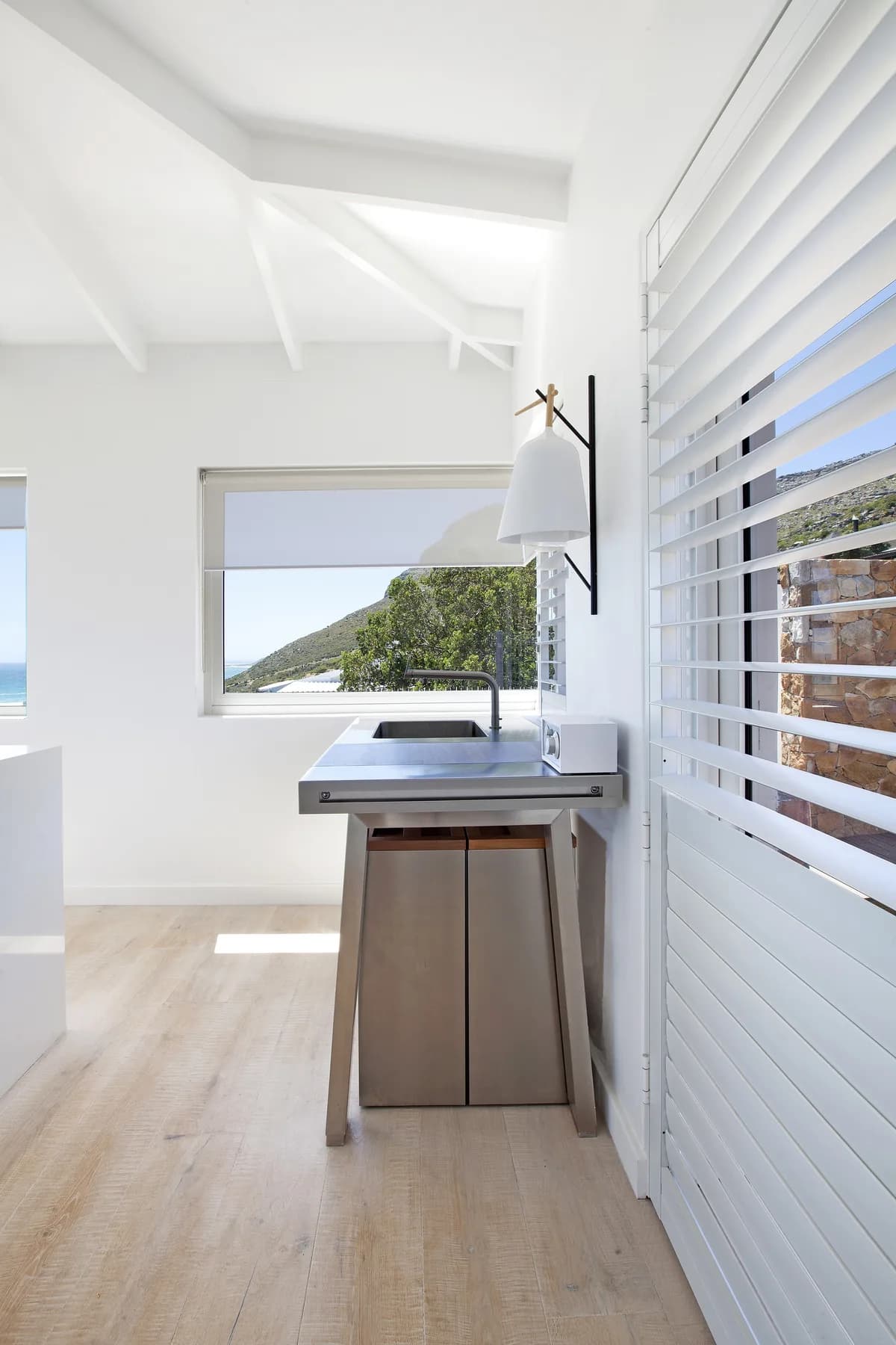 White ShutterGuard louvre shutter beside a kitchen with an ocean view