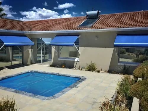Three blue fall arm awnings extended over windows beside a pool